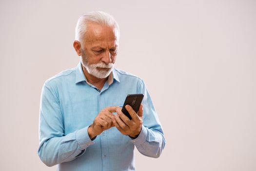 Portrait of cheerful senior man who is using smartphone.