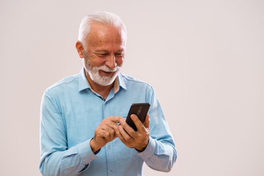 Portrait of cheerful senior man who is using smartphone.