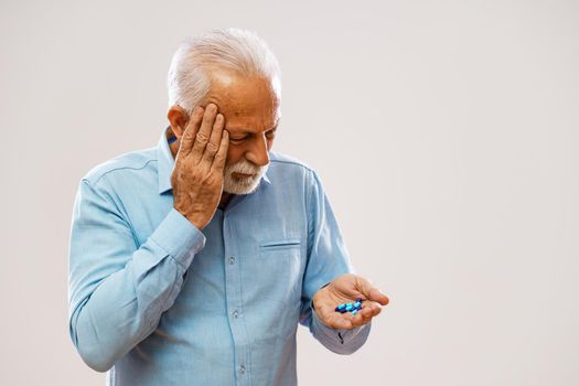 Portrait of serious senior man who is having headache and holding pills.