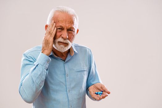 Portrait of serious senior man who is having headache and holding pills.