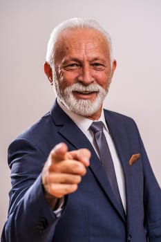 Portrait of happy senior businessman who is pointing at you.