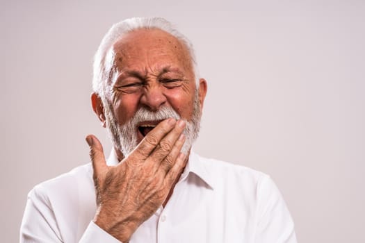 Portrait of tired senior man who yawns.