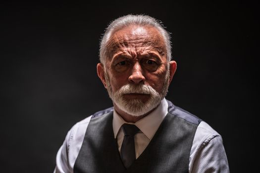 Portrait of serious senior man on black background.