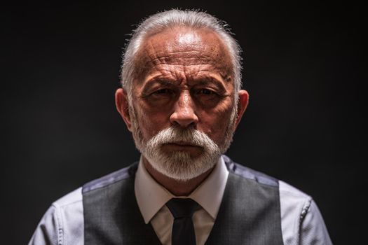 Portrait of serious senior man on black background.