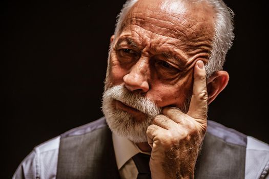 Portrait of pensive senior man on black background.