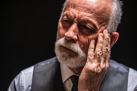 Portrait of pensive senior man on black background.