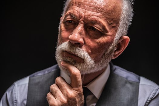 Portrait of pensive senior man on black background.
