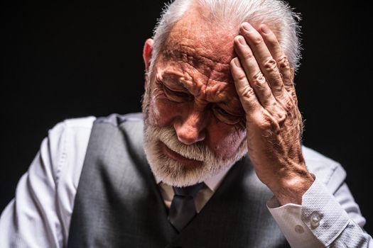 Portrait of depressed senior man on black background.