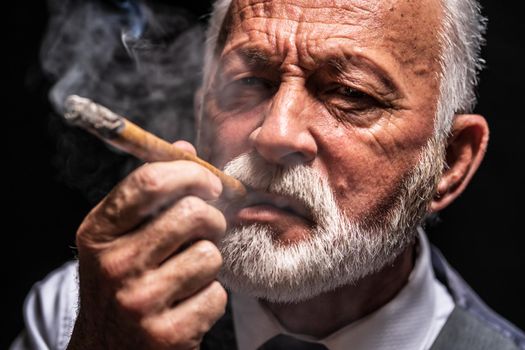 Portrait of serious senior man who is smoking cigar.