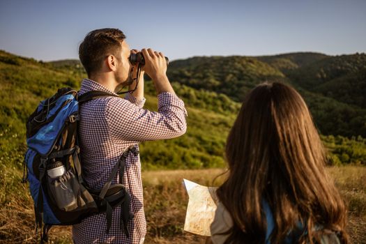 Happy couple is hiking in mountain. They are looking at map.