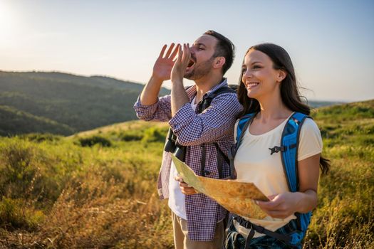 Happy couple is hiking in mountain. They are looking at map.