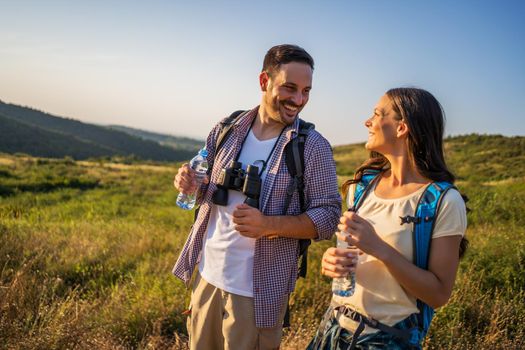 Couple is hiking in mountain. They are drinking water.