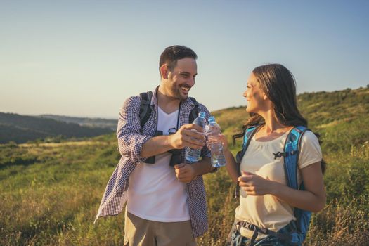 Couple is hiking in mountain. They are drinking water.