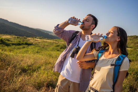 Couple is hiking in mountain. They are drinking water.