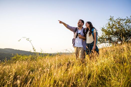 Happy couple is hiking in mountain. They are watching nature with binoculars.