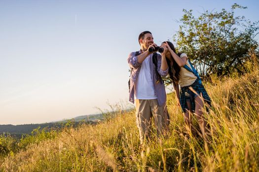 Happy couple is hiking in mountain. They are watching nature with binoculars.