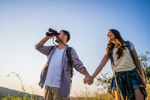 Happy couple is hiking in mountain. They are watching nature with binoculars.