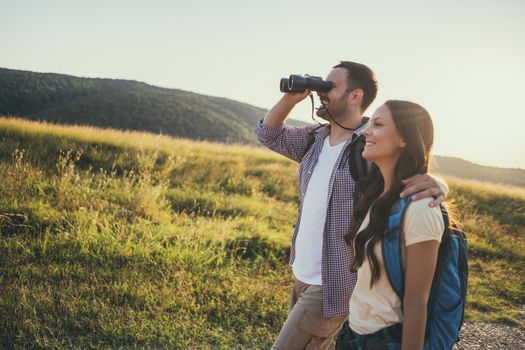 Happy couple is hiking in mountain. They are watching nature with binoculars.