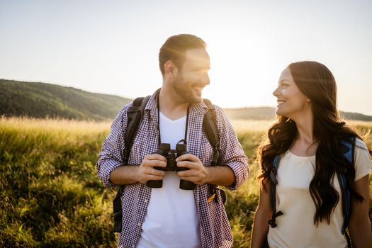 Happy couple is hiking in mountain. They are watching nature with binoculars.