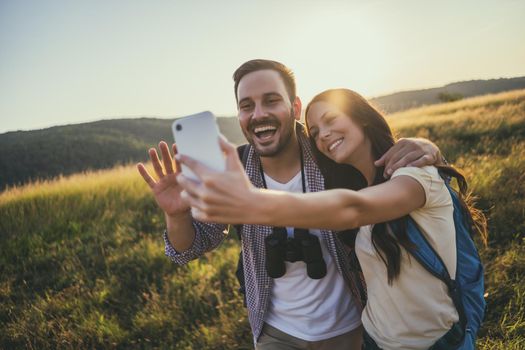 Happy couple is hiking in mountain. They are taking selfie.