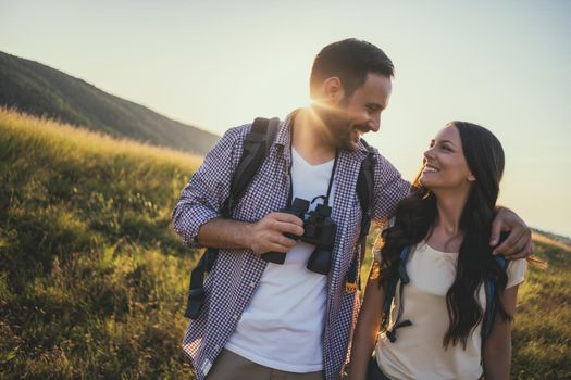 Happy couple is hiking in mountain. They are watching nature with binoculars.