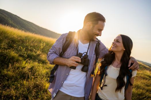 Happy couple is hiking in mountain. They are watching nature with binoculars.