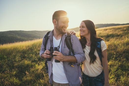 Happy couple is hiking in mountain. They are watching nature with binoculars.