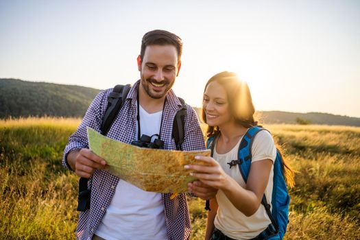 Happy couple is hiking in mountain. They are looking at map.