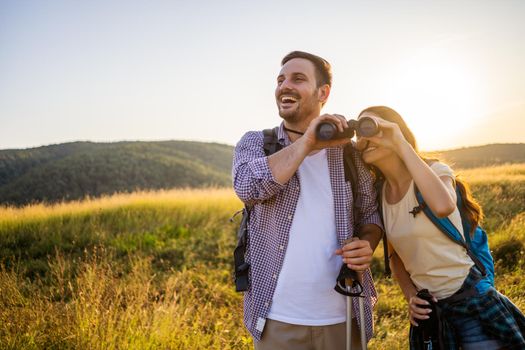 Happy couple is hiking in mountain. They are watching nature with binoculars.