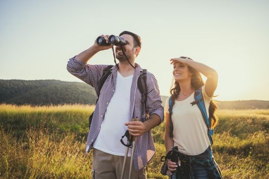 Happy couple is hiking in mountain. They are watching nature with binoculars.