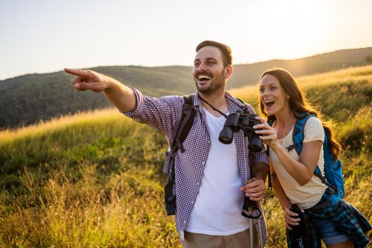 Happy couple is hiking in mountain. They are watching nature with binoculars.