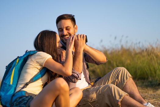 Happy couple is hiking in mountain. They are watching nature with binoculars.