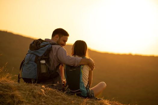 Young happy couple is hiking in mountain and enjoying sunset.