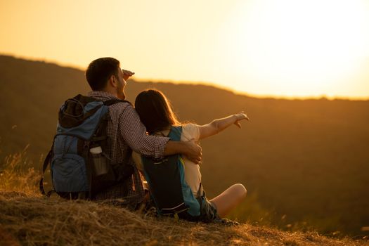 Young happy couple is hiking in mountain and looking at sunset.