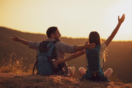 Young happy couple is hiking in mountain and looking at sunset.