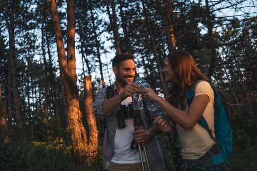 Young couple is hiking in forest. They are drinking water.