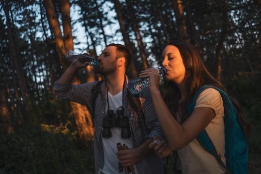 Young couple is hiking in forest. They are drinking water.