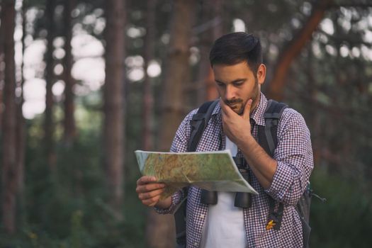 Adult man is hiking in forest. He is looking at map.