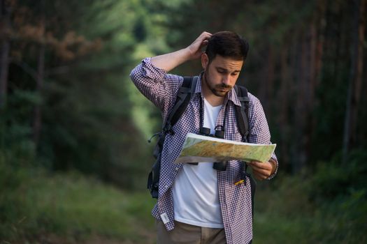 Adult man is hiking in forest. He is looking at map.