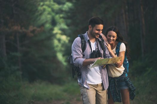 Happy couple is hiking in forest. They are looking at map.