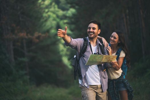 Happy couple is hiking in forest. They are looking at map.