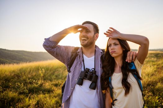 Happy couple is hiking in mountain. They are watching nature with binoculars.