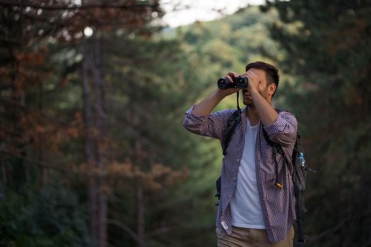 Happy adult man is hiking in forest. He is using binoculars.