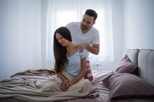 Young couple is waking up in the morning. Woman has pain in neck.