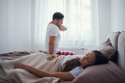 Young couple is waking up in the morning. Man has pain in neck.