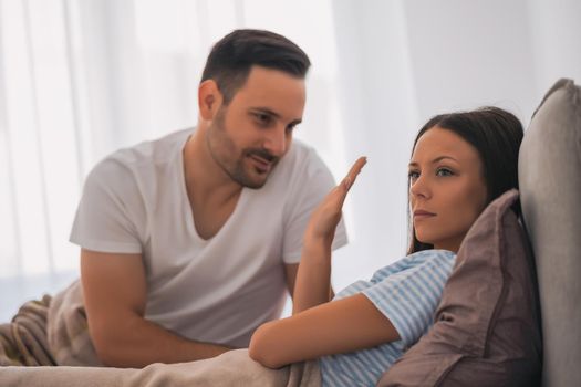 Young couple is arguing in bed. Woman is offended and angry.