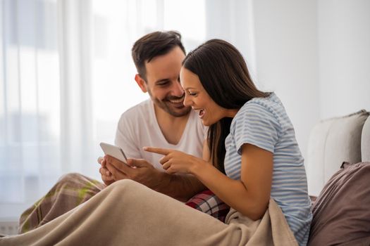 Young happy couple is looking at smartphone in bed in the morning.