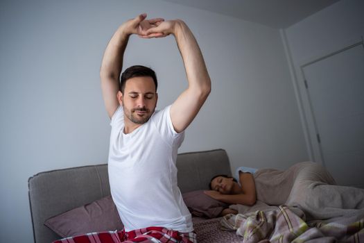 Young couple is sleeping in bed. Man is waking up for work.