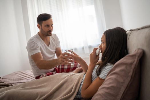 Woman is sick, man is giving her pills.