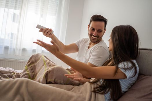 Young couple is watching tv in their bedroom.